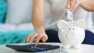 Young woman putting money in a piggy bank and using a calculator