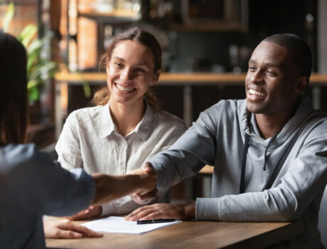 Happy young interracial couple shake hand of bank manager broker buy insurance services take mortgage loan, mixed ethnicity customers handshake agent make agreement financial business deal at meeting