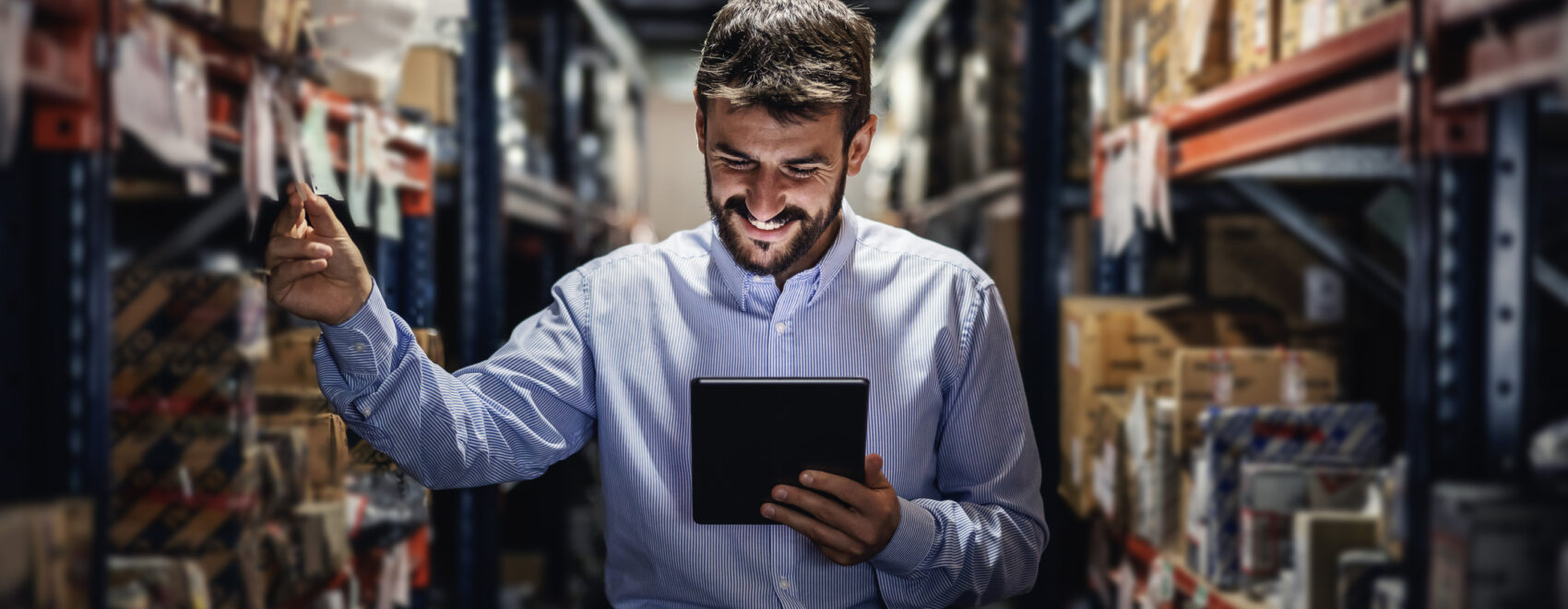 Smiling bearded supervisor standing in warehouse full of boxes a