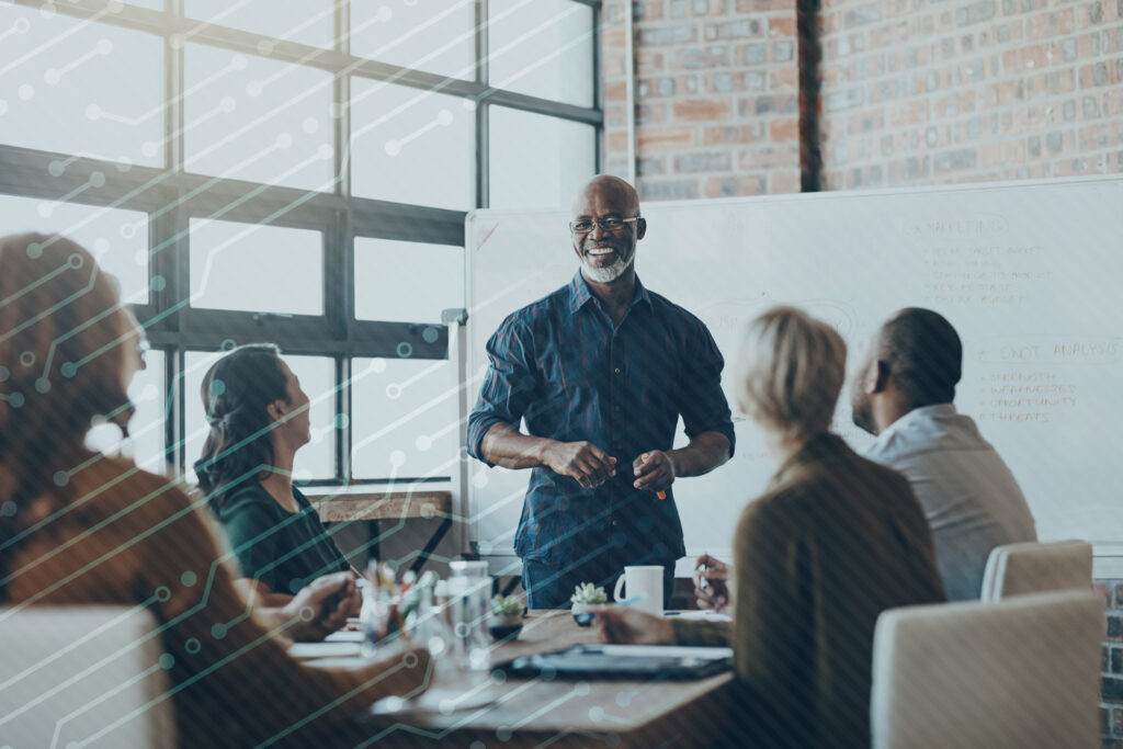 A team of professionals sitting around a table with one of them standing and leading the conversation.